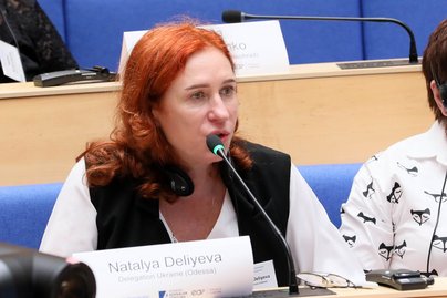 Foto Natalya Deliyeva in einem Plenarsaal, sie spricht ins Mikrofon.