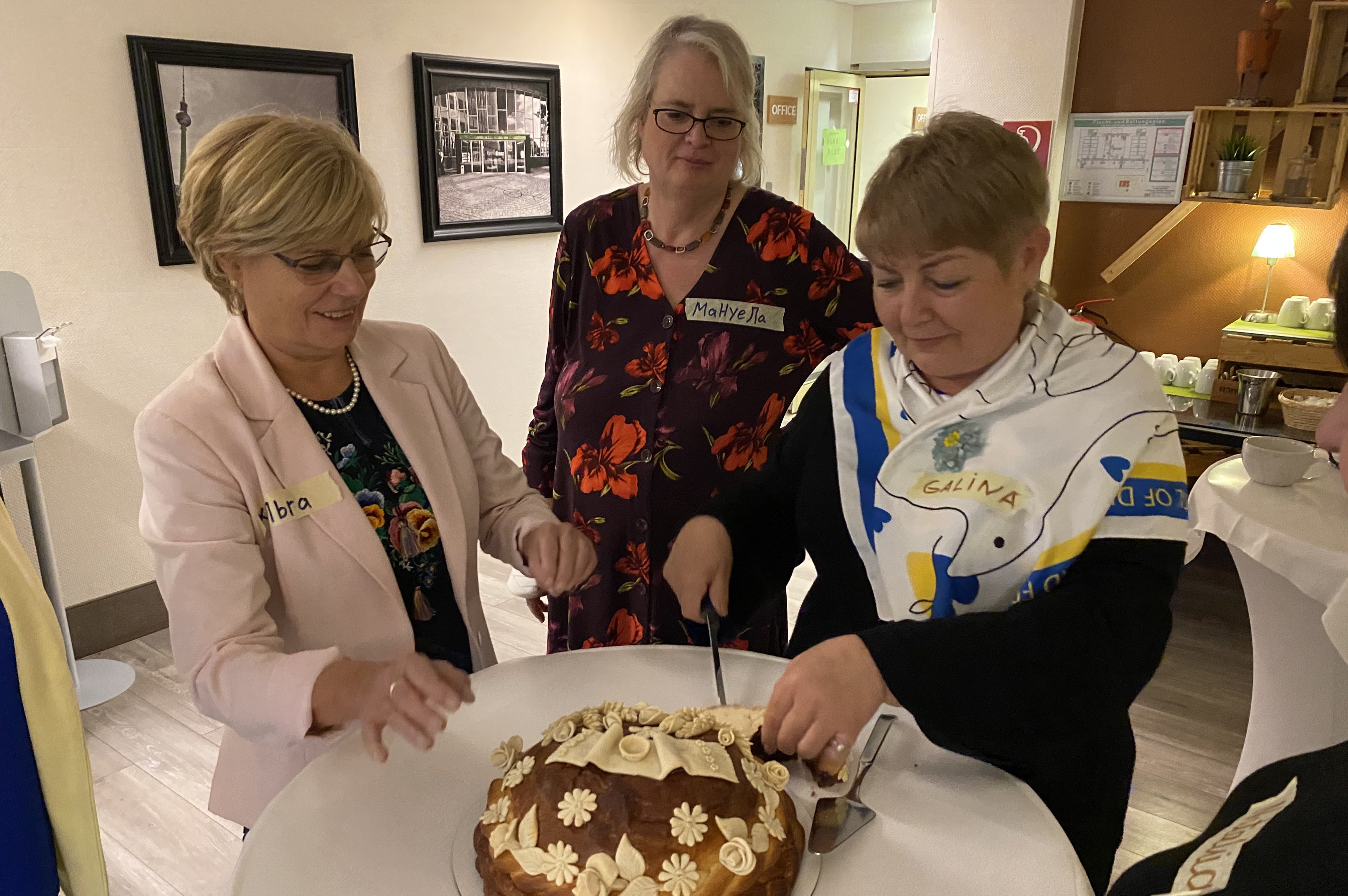 Ein kuchen wird angeschnitten, drei Frauen stehen um einen Stehtisch.
