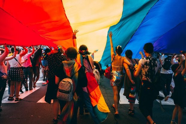 Viele Personen laufen unter einer riesigen Regenbogen-Flagge.