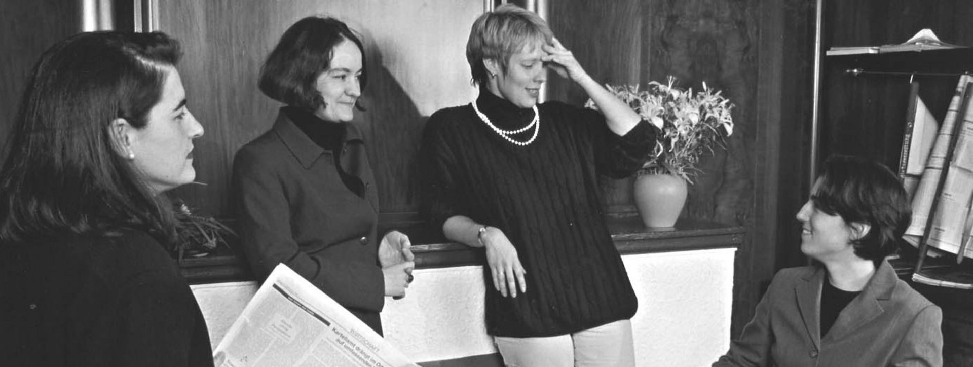 Ein schwarz-weiß Foto mit 4 Frauen, die sich unterhalten. 3 von ihnen stehen, eine sitzt.